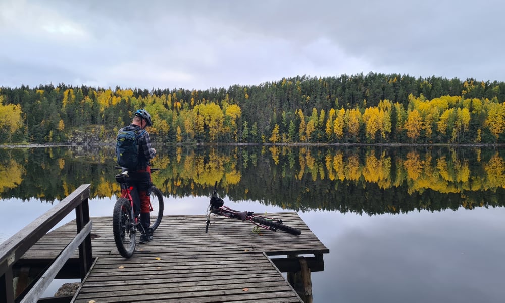 Syksyisessä kuvassa mies laiturilla pyörän kanssa. Taustalla vettä ja syksyisiä puita keltaisine lehtineen.