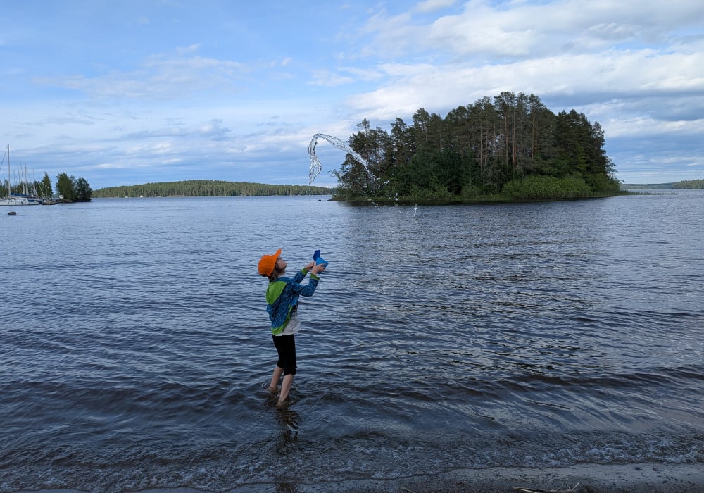 Poika heittää ämpäristä vettä ilmaan hiekkarannalla.